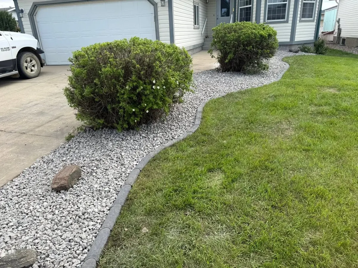 A curved stone border holding a rock bed of trimmed shrubs along a driveway